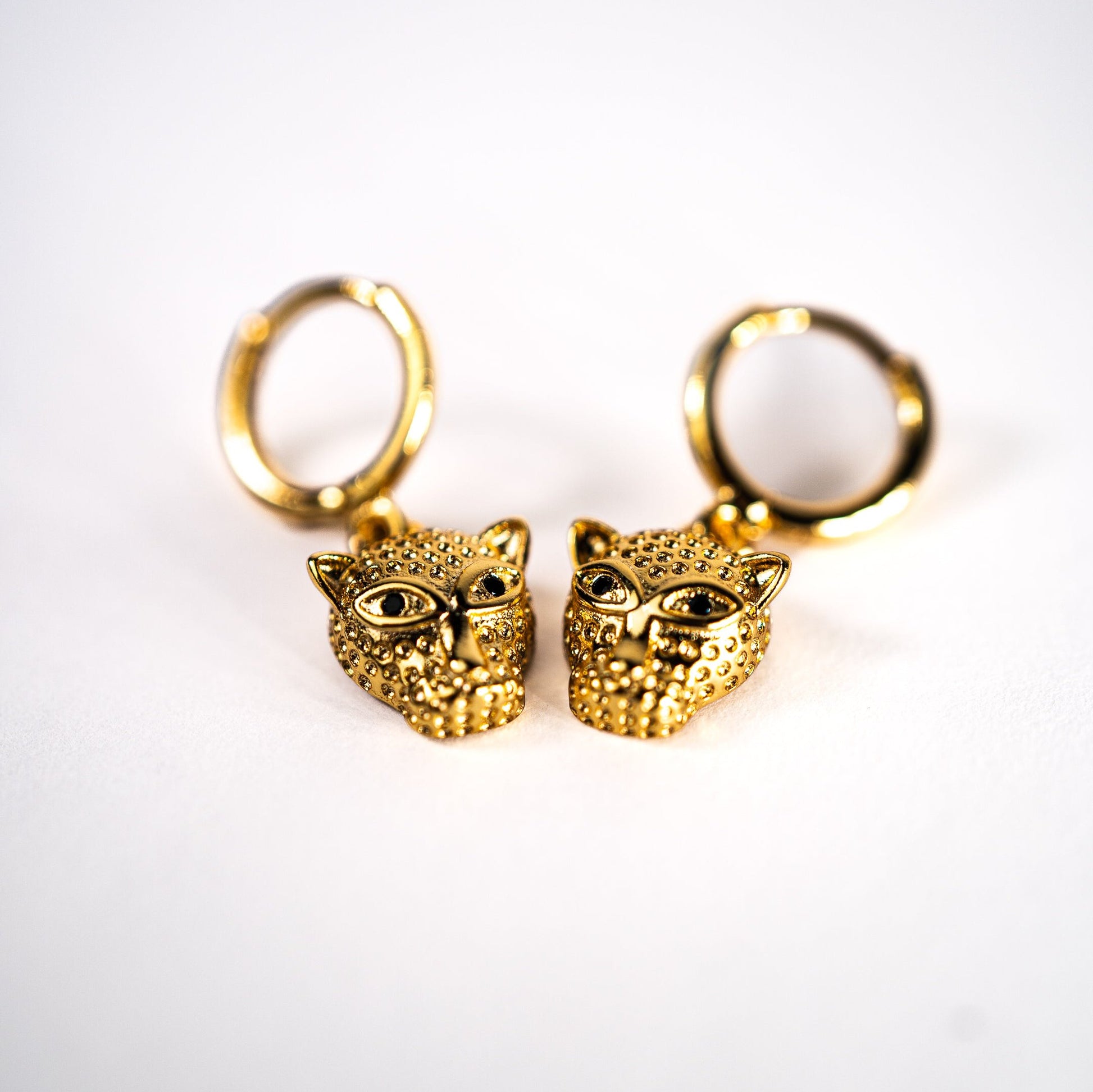 Leopard drop hoop earrings, Lula Sea Jewellery New Zealand, gold hoop earrings featuring a small leopards head pendant hanging from them pictured on flat surface. Gold plated