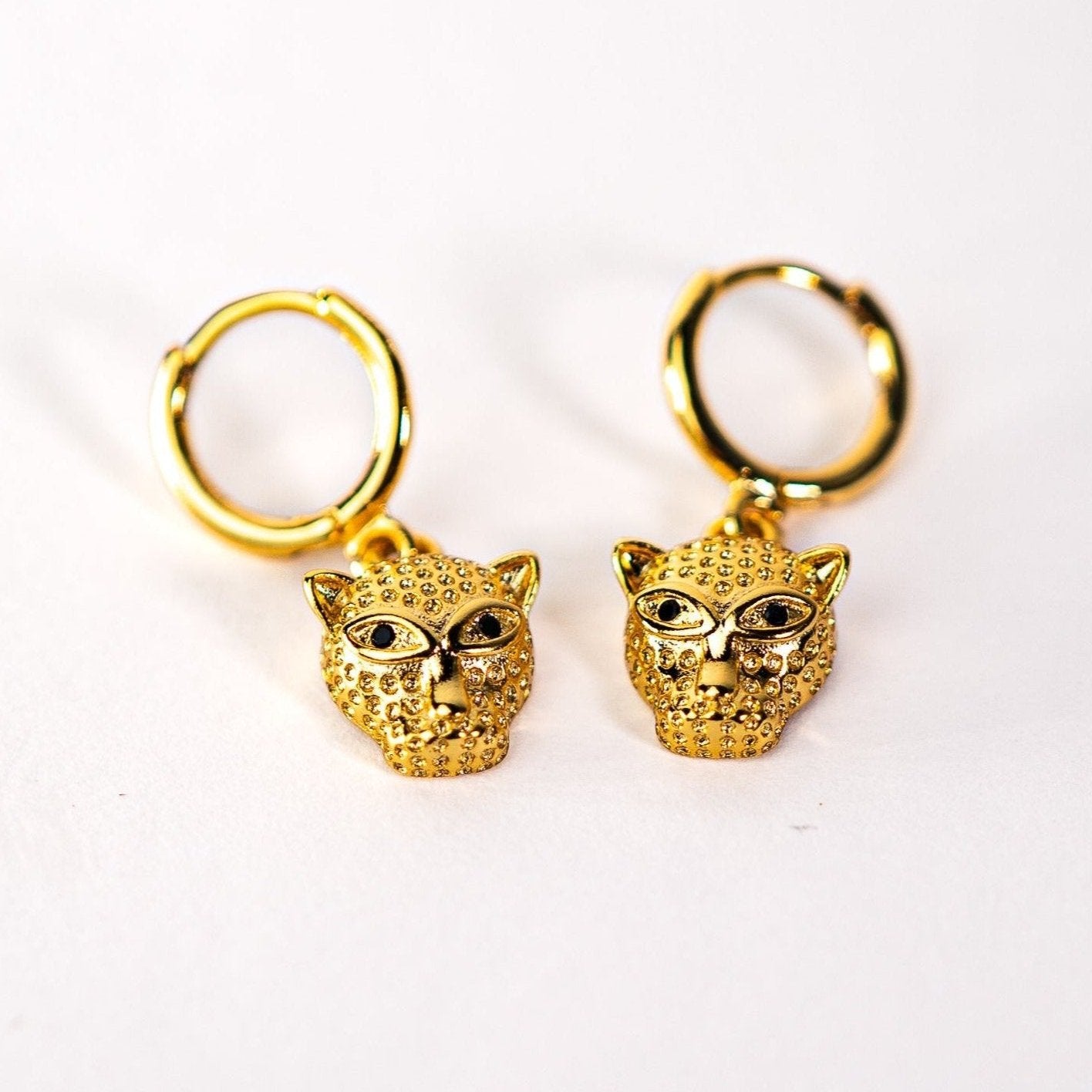 Leopard drop hoop earrings, Lula Sea Jewellery New Zealand, gold hoop earrings featuring a small leopards head pendant hanging from them pictured on flat surface. Gold plated