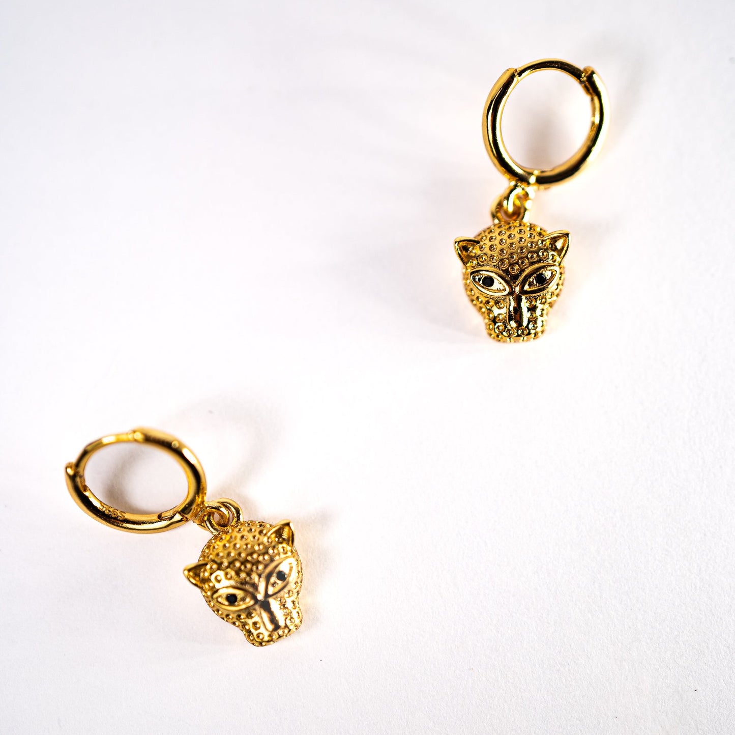 Leopard drop hoop earrings, Lula Sea Jewellery New Zealand, gold hoop earrings featuring a small leopards head pendant hanging from them pictured on flat surface. Gold plated